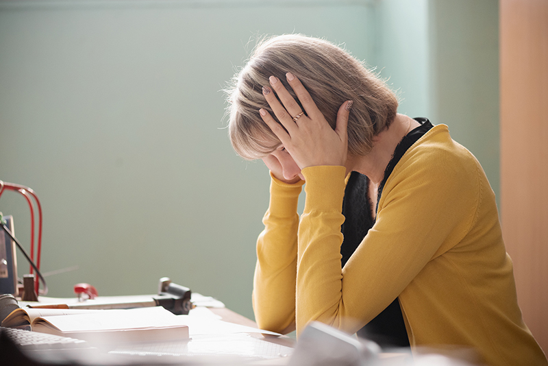 Image of frustrated female teacher sitting at a desk and holding her head.