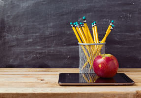 Back to school background with tablet, pencils and apple over chalkboard